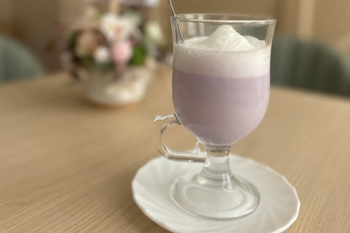 Ube latte tejhabbal, talpas üvegpohárban, tányéron